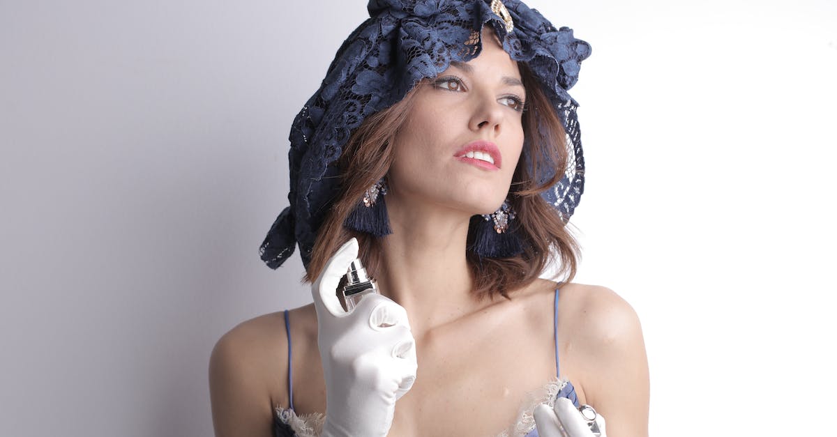 What headgear reduces prices the most? - Charismatic sensual female in elegant vintage blue dress and lace headgear wearing white satin gloves and luxury bijouterie looking away and spraying fragrant perfume to delicate neck skin against white background