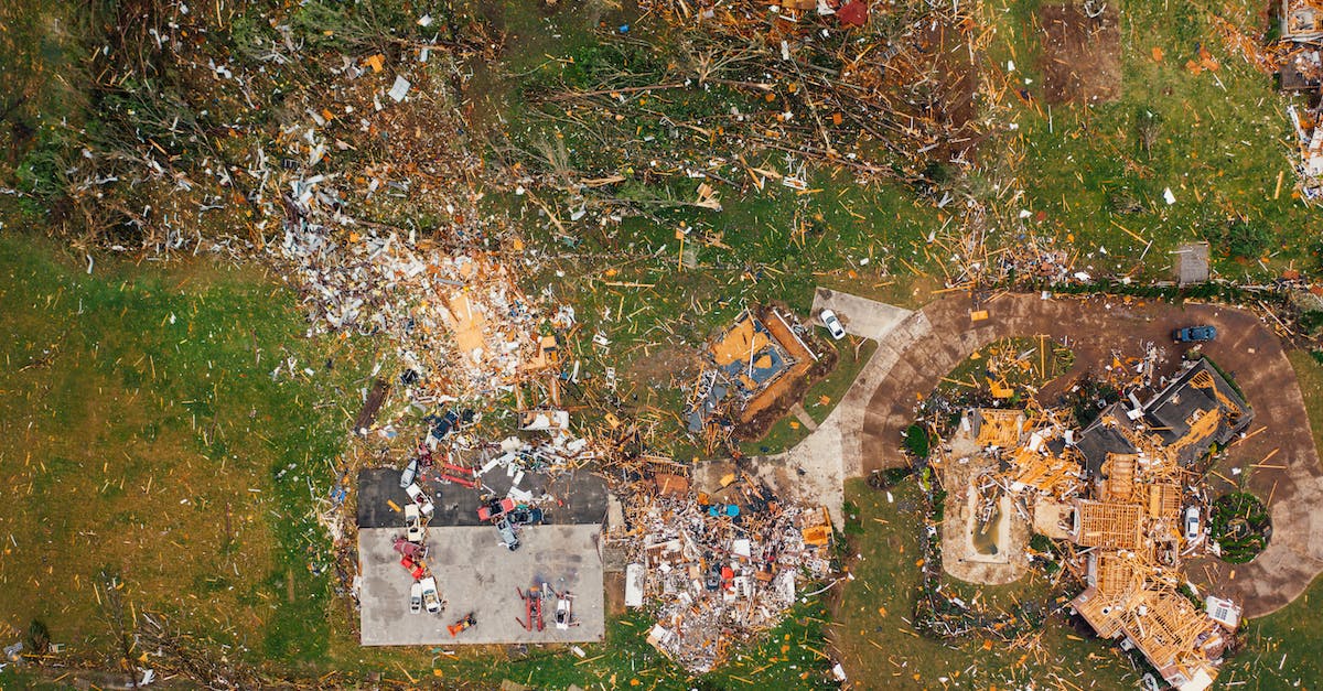 What impact is there to bulldozing housing? - Aerial view of dramatic consequences of massive hurricane with ruined houses and kindling woods lying on green lawn