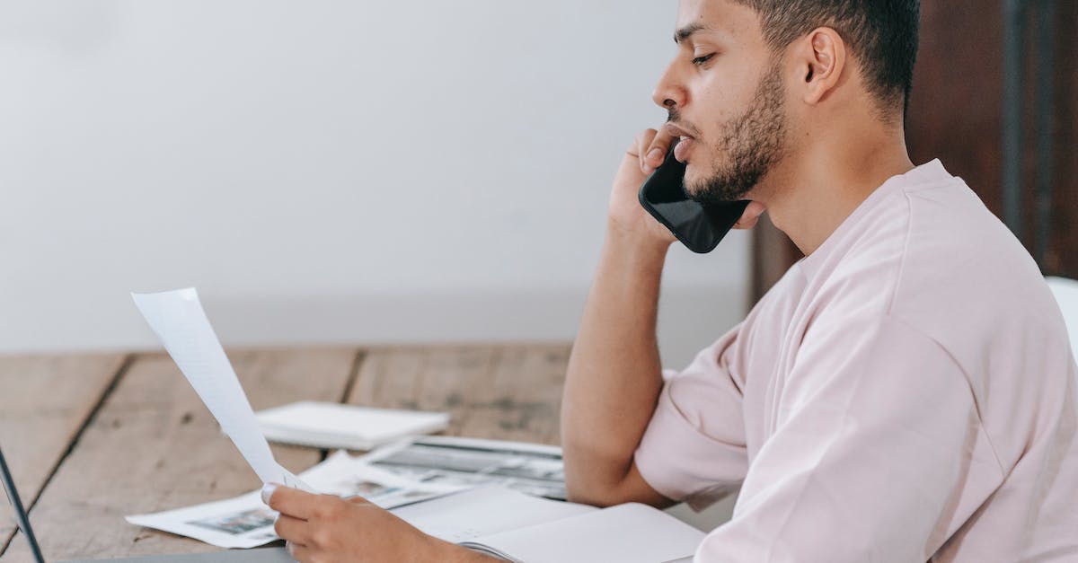 What is it called to check your co-ordinates on Minecraft? - Side view of young Hispanic male remote employee discussing documents during phone call while working online with laptop and papers in home office
