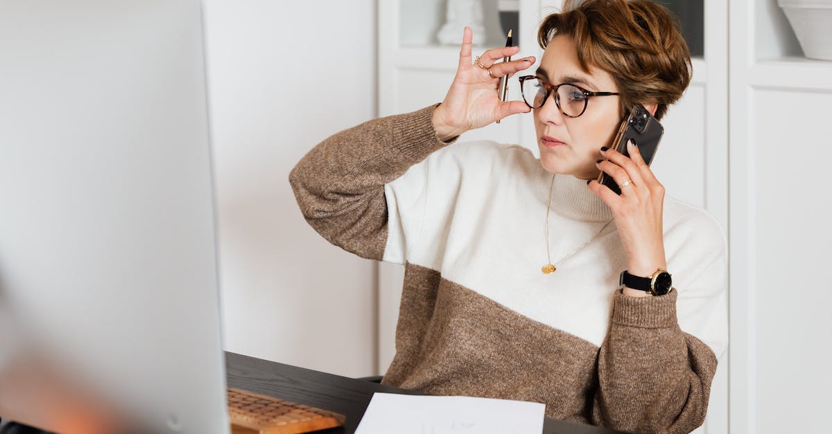 What is it called to check your co-ordinates on Minecraft? - Serious good looking woman in glasses talking on smartphone and looking at computer screen with pen in hand and sheet of paper on desk