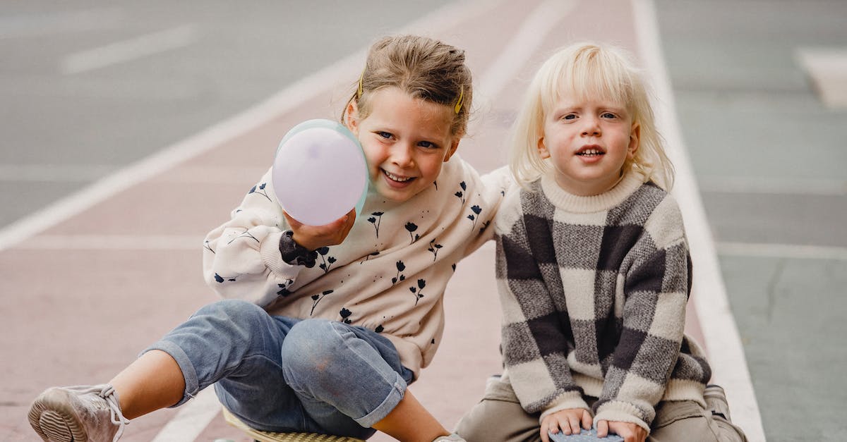 What is the blue/grey balloon on Happy Street? - Full body of smiling children in casual wear sitting on skateboards on asphalt road in daytime