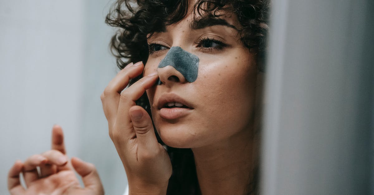 What is the fewest cycles to clear Majora's Mask, without exploiting glitches? - Mirror reflection of young female with curly hair putting nose strip mask on face in bathroom
