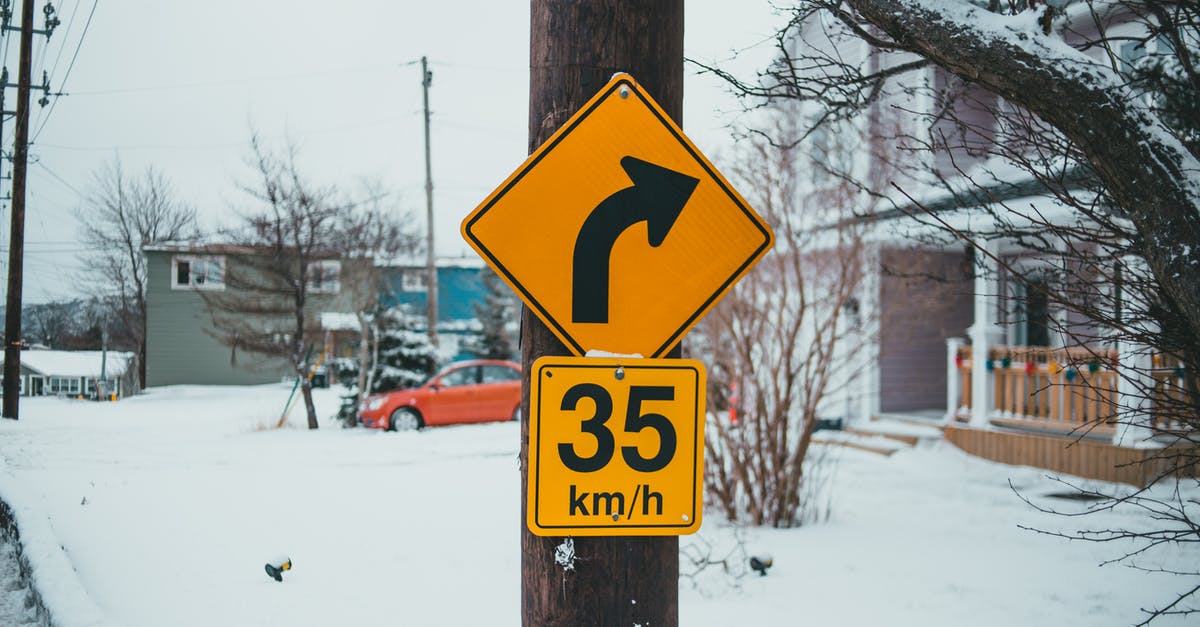 What is the limit on the number of students you can recruit into your house? - Control road signs with arrow showing turn under speed limit on post against buildings with snow in wintertime