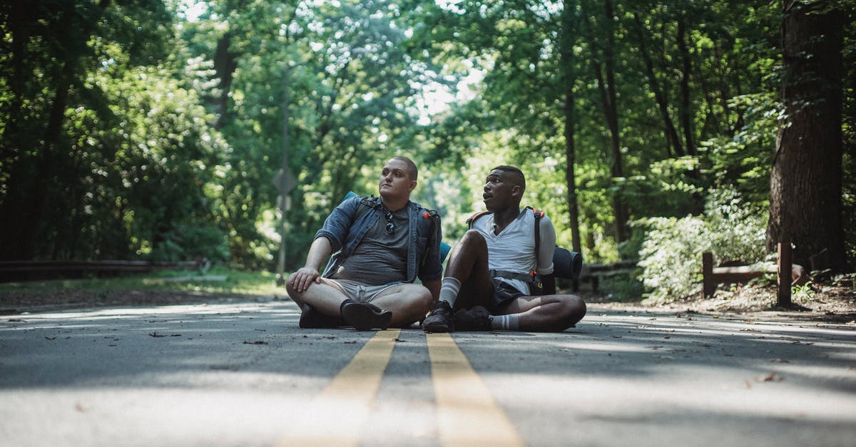 What is the most effective way to help a friend leveling up? - Pensive diverse hikers with backpacks sitting on asphalt roadway in countryside and looking away What is the most effective way to help a friend leveling up? - Pensive diverse hikers with backpacks sitting on asphalt roadway in countryside and looking away