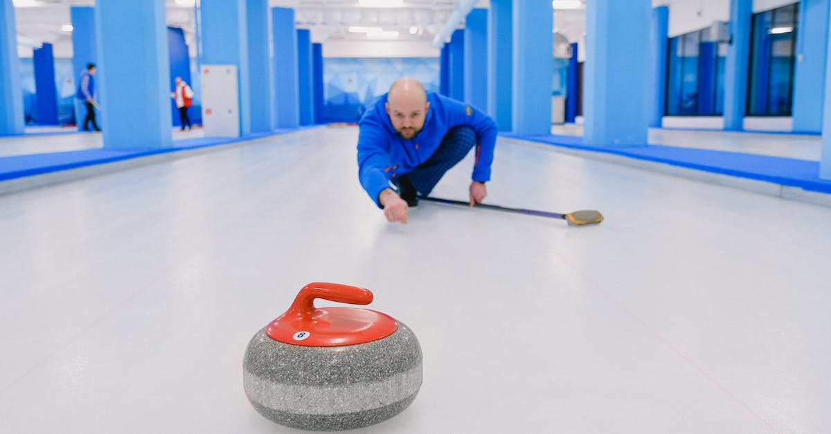 What is the name of the game mechanic in which the player "slides" towards obstacles? - Focused sportsman in blue activewear standing on knee with broom stick and looking at sliding stone during curling training on ice rink