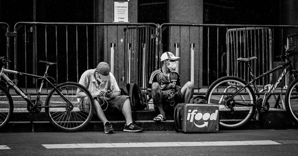 What is the period after a game's main story line ends called? - Black and white of anonymous delivery male in face masks sitting near fence and roadway with parked bicycles in town during COVID 19 pandemic What is the period after a game's main story line ends called? - Black and white of anonymous delivery male in face masks sitting near fence and roadway with parked bicycles in town during COVID 19 pandemic