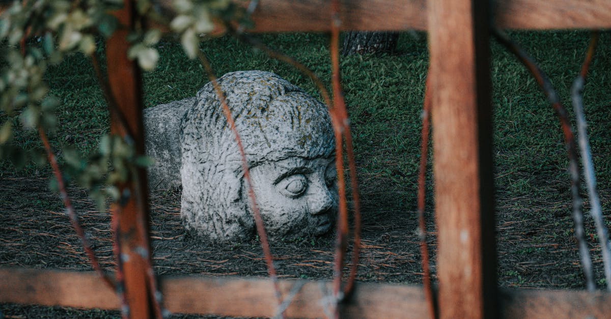 What is the story behind Monument Valley? - Weathered white stone statue of human head located on grassy ground behind wooden fence in park What is the story behind Monument Valley? - Weathered white stone statue of human head located on grassy ground behind wooden fence in park