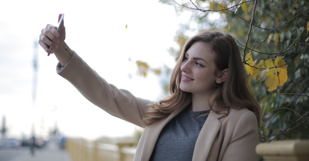 What is the use to the memories that you unlock? - Young woman in coat taking selfie with smartphone on street in overcast weather