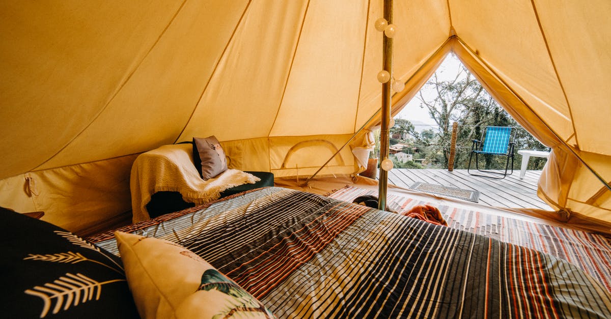 What is this yellow pillar of light from the sky? - Soft bed with colorful blanket and cushions placed in tent with decorated pole and doorway in rural area of countryside