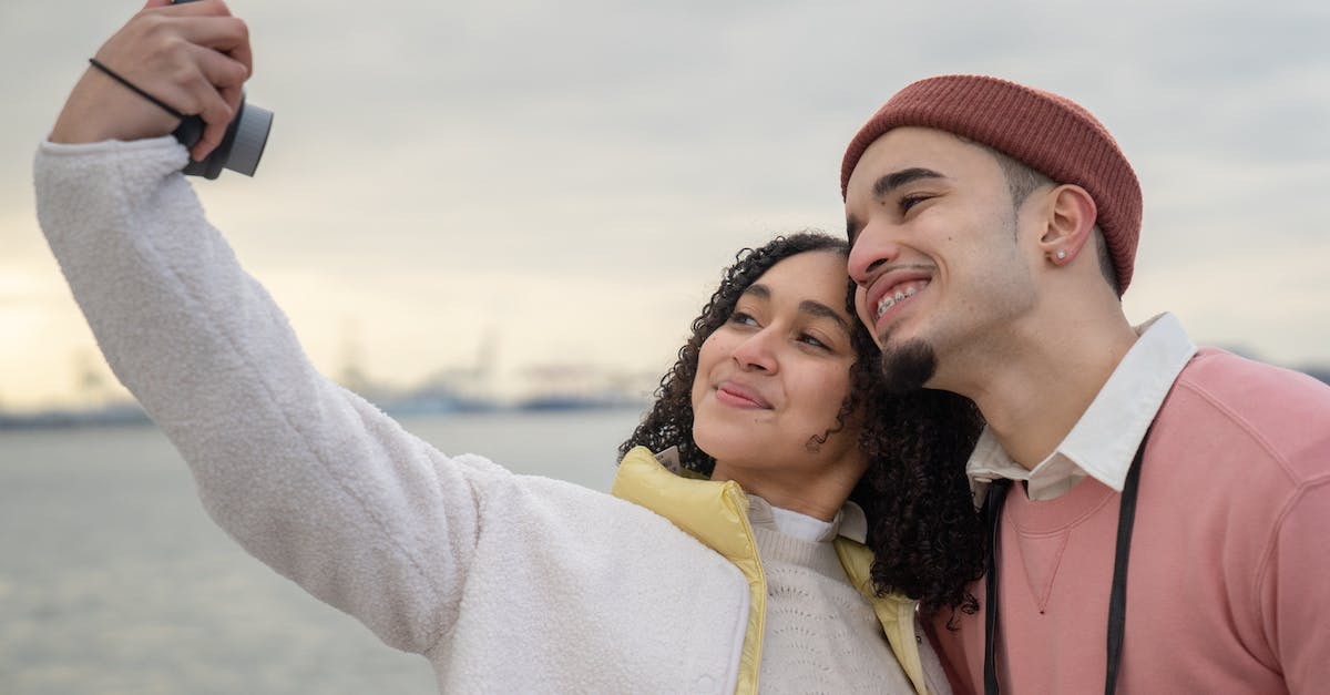 What lubricant does Sony use for the PS3 analog stick? - Smiling Latin American couple in warm clothes standing near river while taking self photo on analog camera in daylight under cloudy gray sky