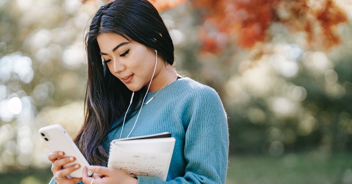 What song is playing in Cassie's earbuds during her intro? - Side view of young smiling Asian female student with notebook and earphones browsing mobile phone in park