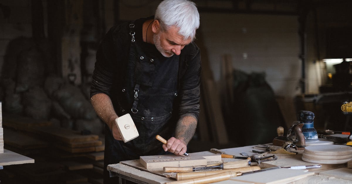 What stickers have special "scratched" patterns? - Serious male woodworker in apron using mallet and chisel to carve wooden board at table with abundance of instruments in carpentry