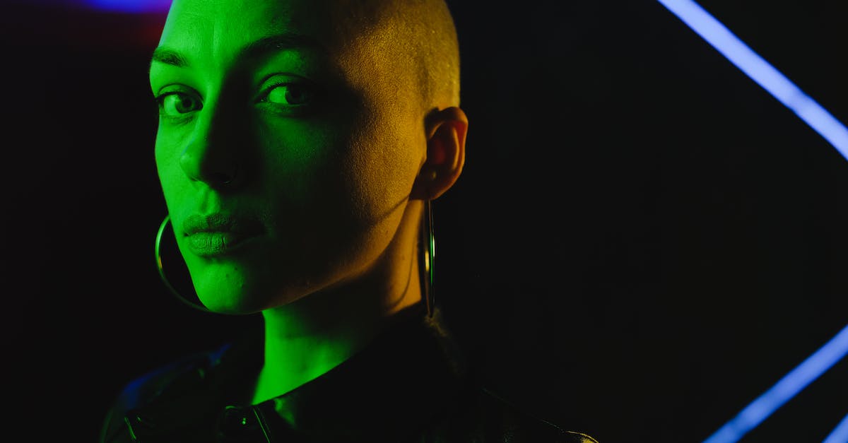 What unusual effects can taunts come in? - Crop unemotional bald female in black lather shirt looking at camera and standing in green neon light in darkness