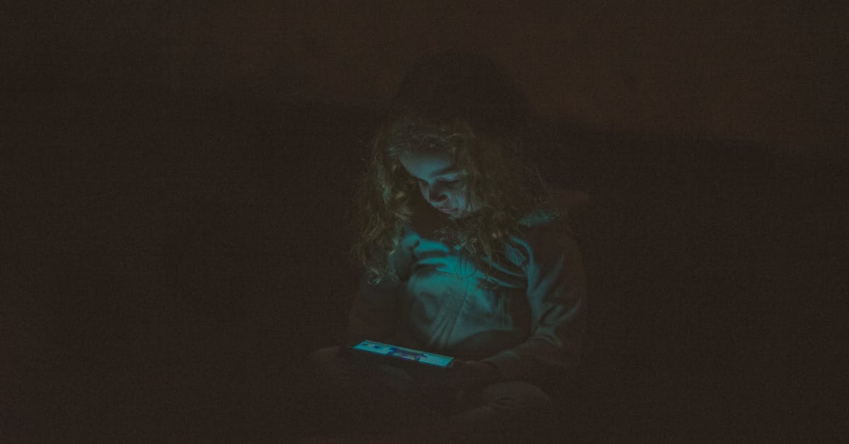 When does mid / late game phase begins? - Focused  little girl with long curly hair in casual clothes sitting and using smartphone while watching video in dark room