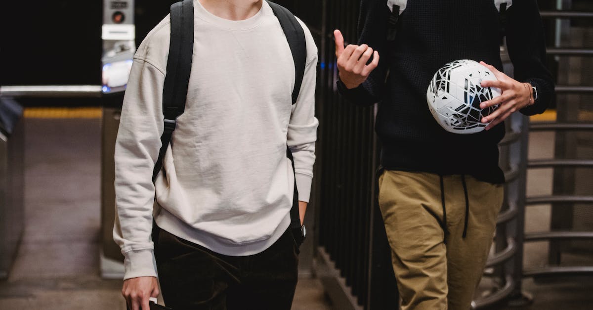 When does time pass in Norende? - Crop young male friends wearing casual clothes with backpacks and soccer ball walking in modern underground station and chatting