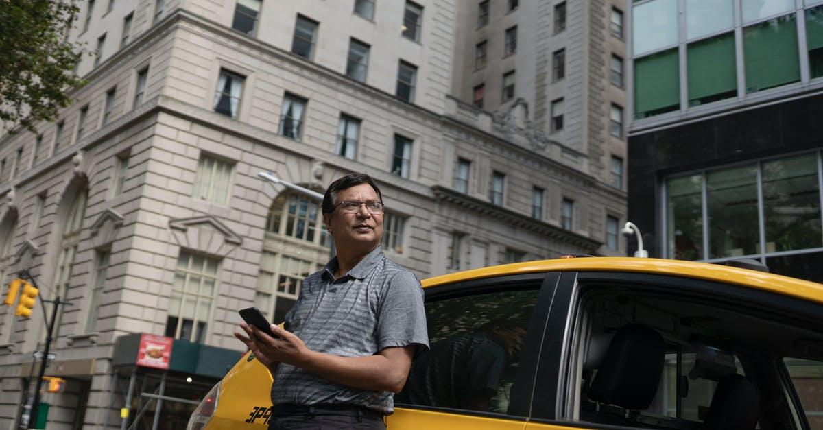 When stealing from cars, should I check the visor? - Low angle of serious ethnic male scrolling mobile phone while leaning on yellow car in downtown
