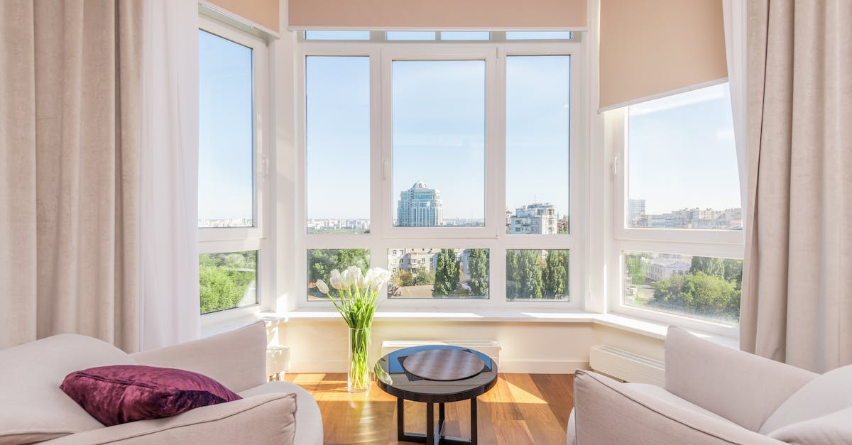 When will my home be furnished? - Interior of modern penthouse with comfortable white armchairs and round side table placed near windows overlooking city in sunny day