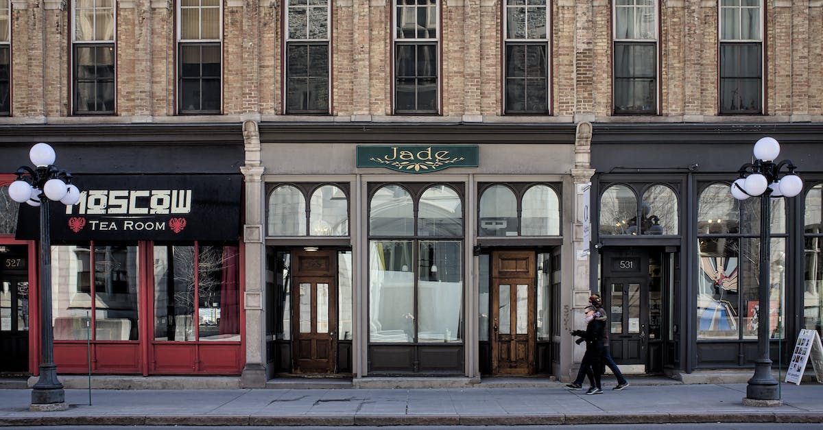 Where are all the shops located? - Woman in Black Coat Standing in Front of Brown Concrete Building