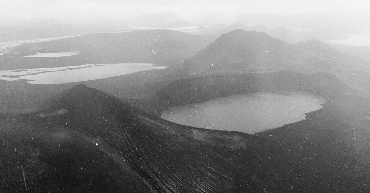 Where are the last survival caches in Geothermal Valley? - Drone view of geothermal crater lake surrounded by volcanic mountains during snowfall in Iceland