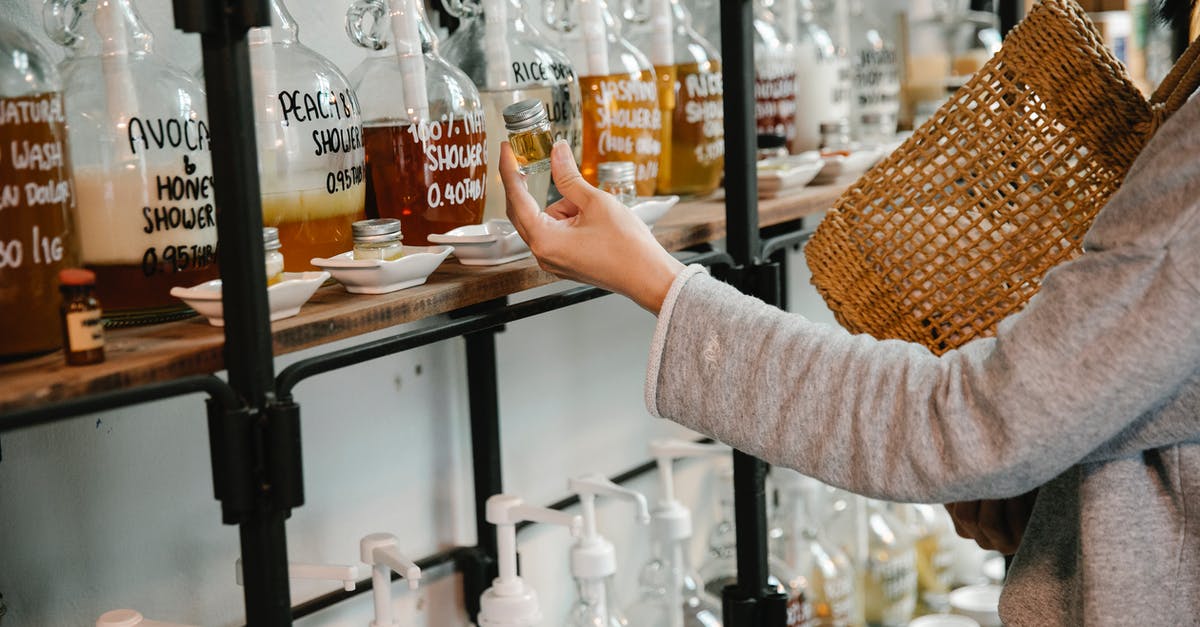 Where can I store my cosmetic gear? - Crop customer examining glass jar with shampoo in market while standing near big dispensers placed on wooden shelves Where can I store my cosmetic gear? - Crop customer examining glass jar with shampoo in market while standing near big dispensers placed on wooden shelves