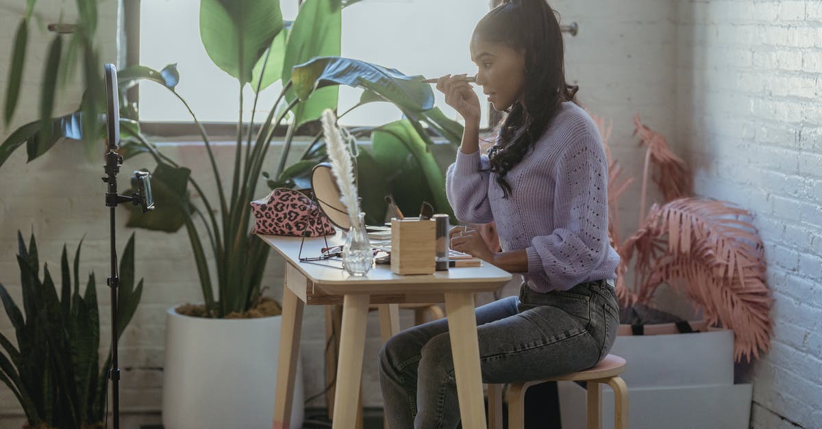 Where do players inside vents appear on the admin table? - Side view of African American woman with long hair in trendy clothes sitting at table with cosmetics and applying makeup while filming vlog in light room