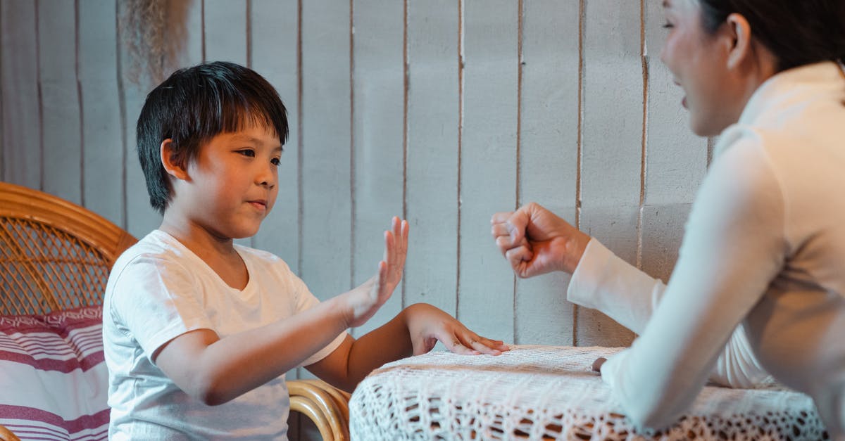 Which was the first game to use multiple Rock Paper Scissors mechanics? - Happy smiling Asian mother and cute boy wearing casual white shirts playing rock paper scissors game against gray plank wall