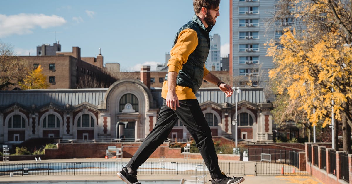 Who is this NPC swimming outside of town borders? - Full body side view of energetic male strolling on edge of concrete border on street during training against residential buildings