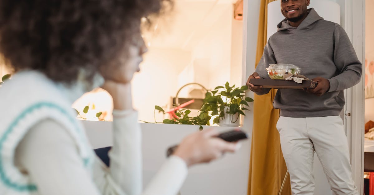 Why are expected delivery times given as a range? - Smiling black man standing in room with bowl of salad near girlfriend sitting on couch