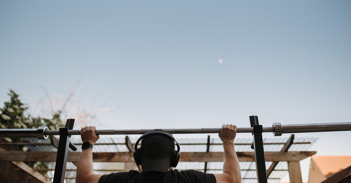 Why aren't trains using all the available stops? - Back view of anonymous muscular male athlete listening to music in headphones while exercising on bar under light sky