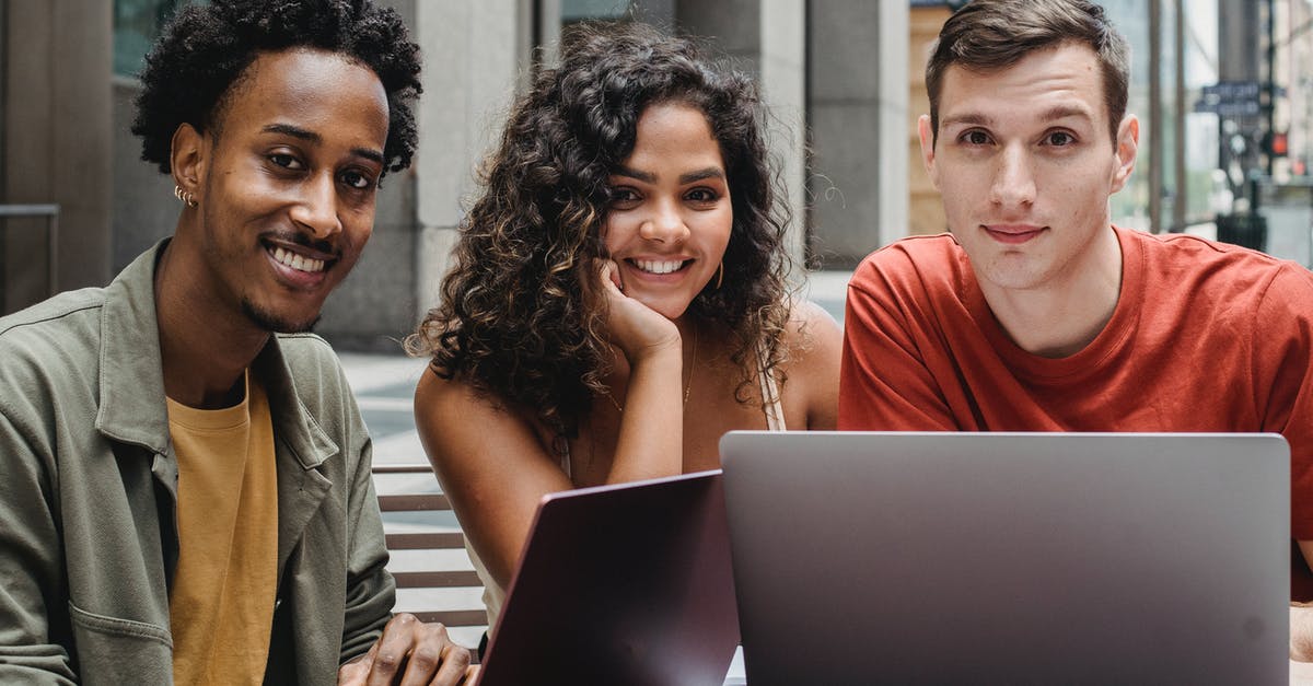 Why can't I summon my friend to help me? - Young multiethnic friends in casual outfit using netbook while sitting at table in city street and looking at camera