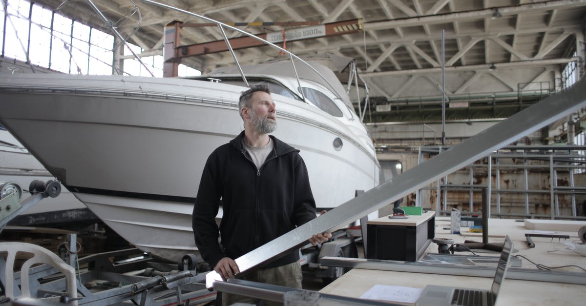 Why can't I use a Robot Workbench at Boston Airport Ruins? - Side view of adult bearded workman in casual clothes standing near workbench and controlling metal detail in garage with yachts
