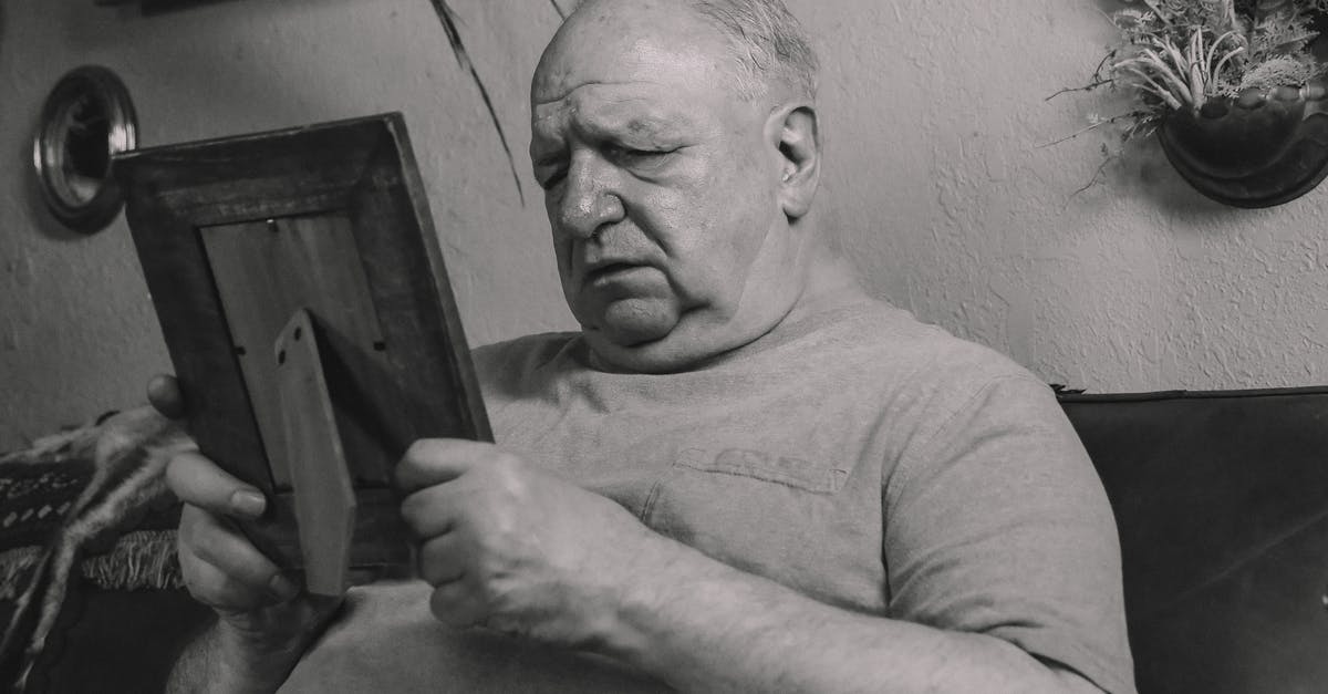 Why citizens are unhappy? - A Grayscale Photo of an Elderly Man Holding a Wooden Frame