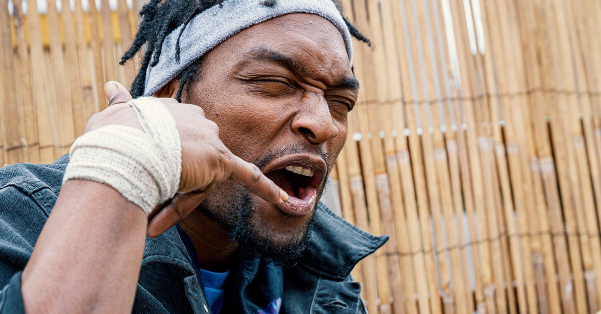 Why did a crazy blob chant &ldquo;One of us, gooble-gooble&rdquo; at me? - Frowning eccentric African American male in casual wear and headband showing call me sign with hand with bandage on wrist while spending time outside