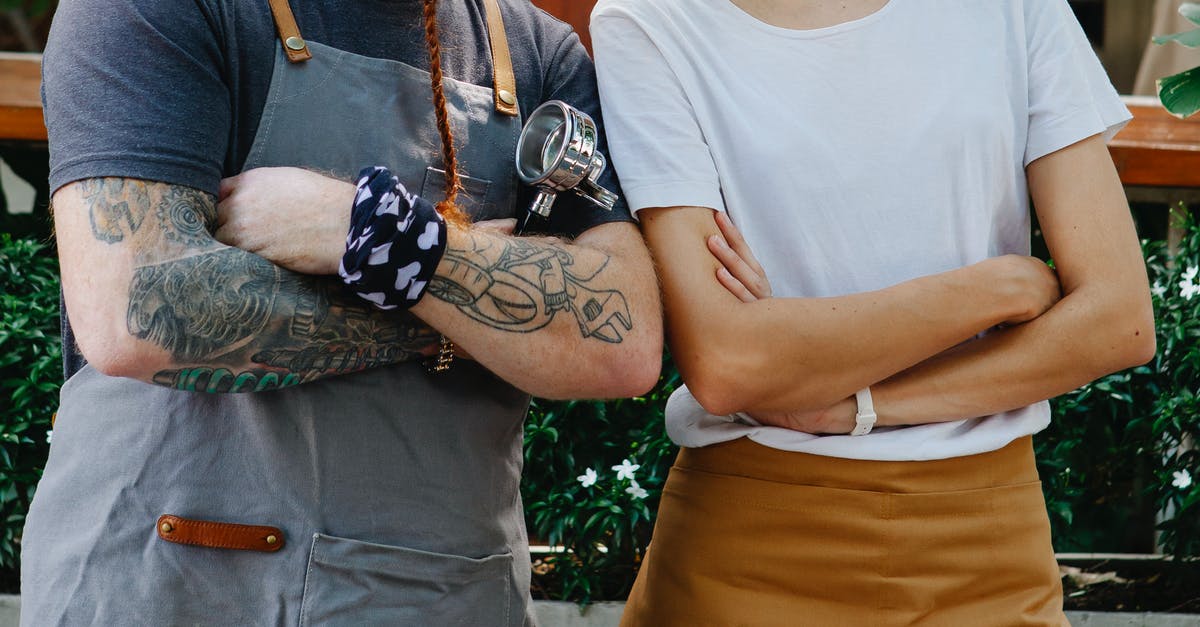 Why do my friends get Tough Break contracts every 15 minutes and I don't? - Crop anonymous couple of barista coworkers in aprons and casual clothes spending time in street with portafilter near plants in daytime