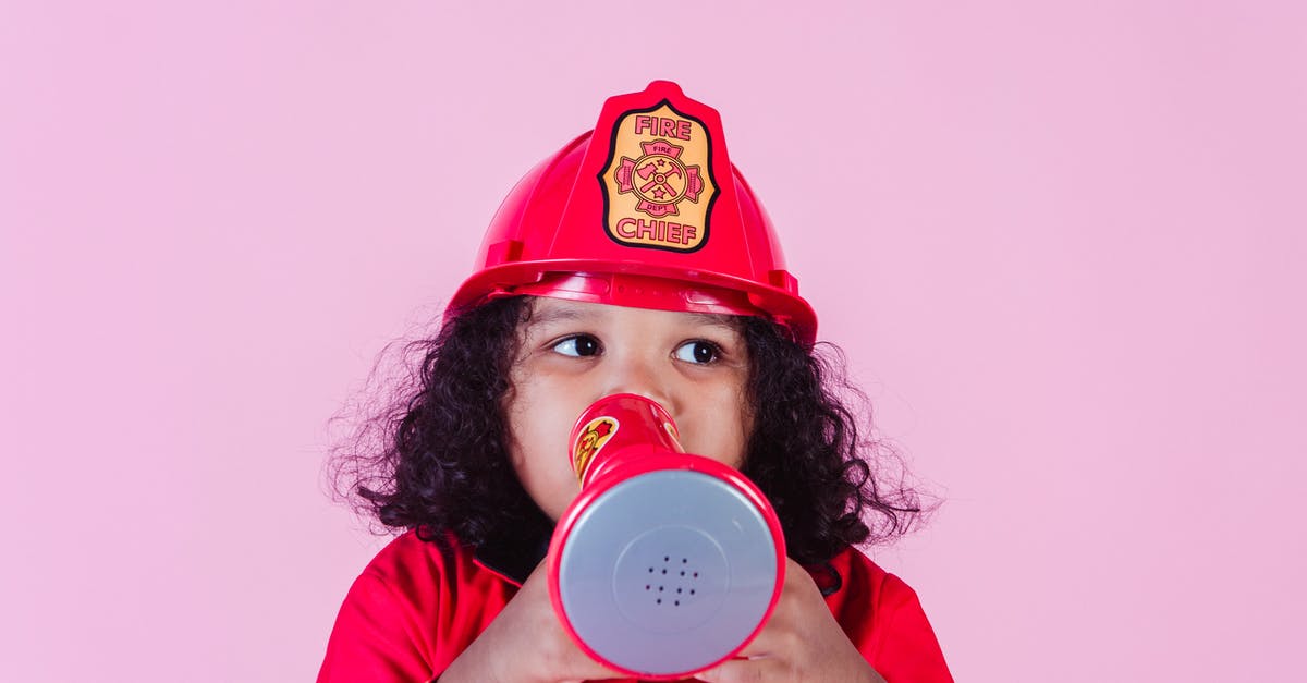 Why do older generations games have a common look and feel by console? - Cute little African American girl wearing bright firefighter costume and helmet and talking in toy loudspeaker while playing in light studio and looking away