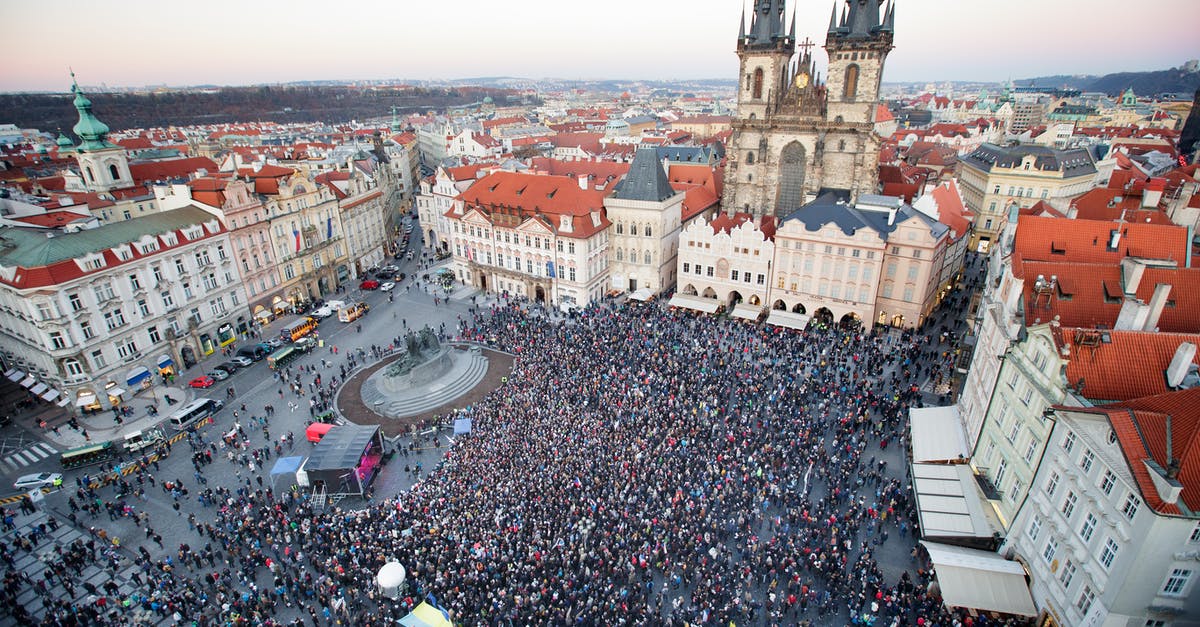 Why have Town Hall outside of farming base? - Drone view of crowd of people standing on square near gothic aged church and old town hall located in Prague