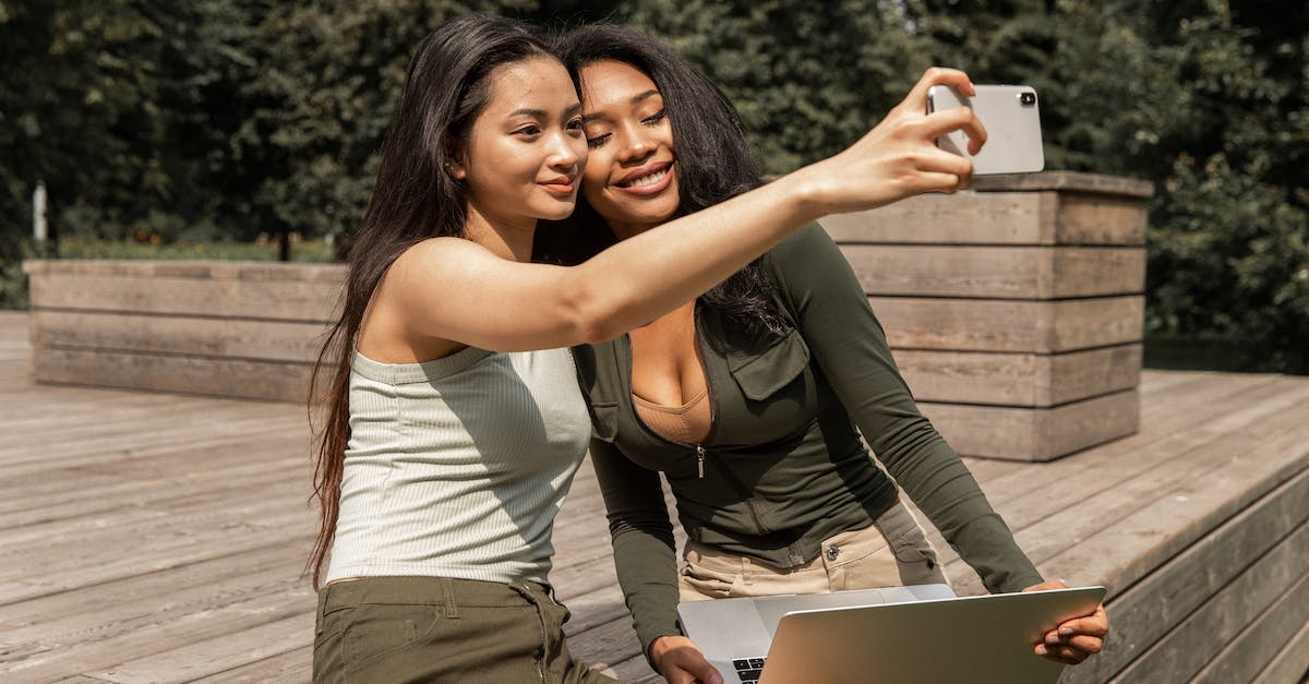 Why is DexNav suddenly taking a long time to find Pokemon? - Positive young multiethnic ladies with long dark hairs in casual outfits smiling and taking selfie on mobile phone while chilling in park with laptop