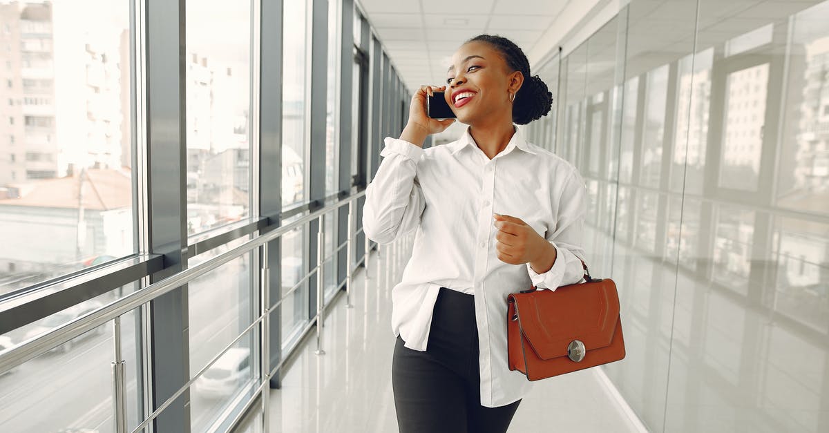 Why is this corridor in Inferno called "Banana"? - Happy black stylish female office worker in formal wear having conversation on mobile phone while strolling along modern building corridor and looking out window