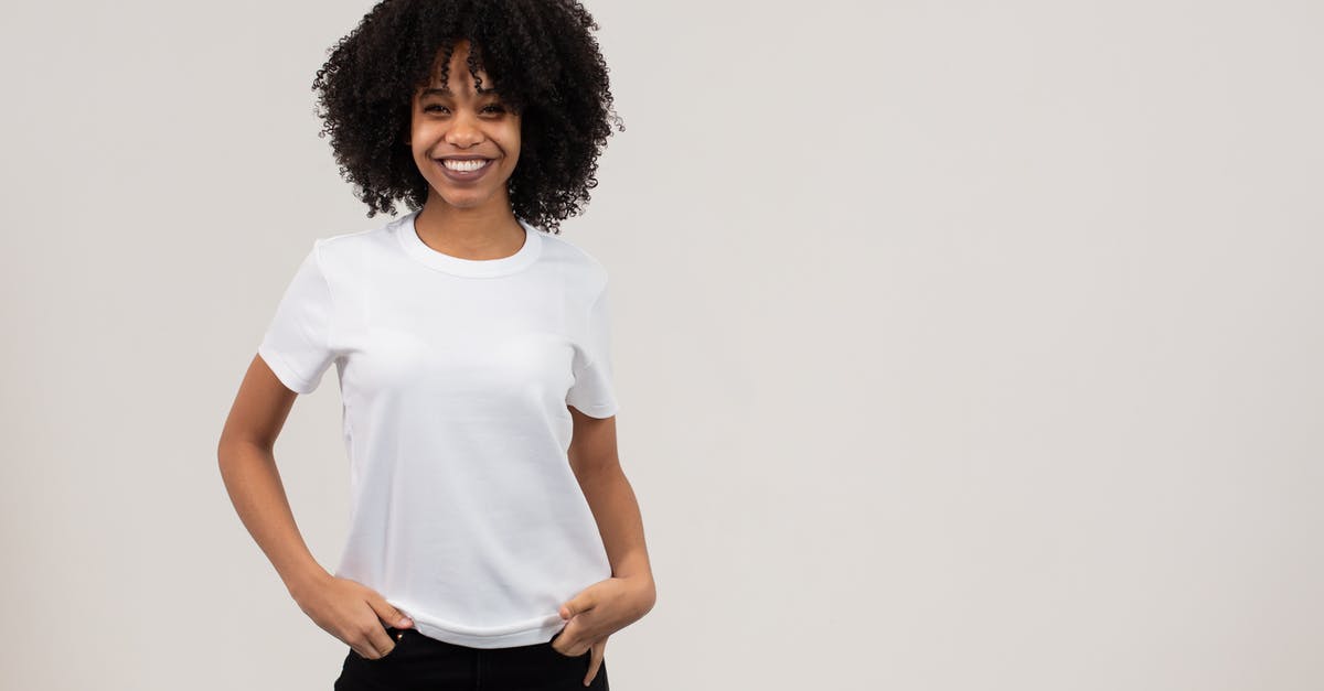 Why isn't Kharjo appearing? - Positive young black female millennial with dark Afro hair in white t shirt smiling and looking at camera while standing in light studio with hands in pockets