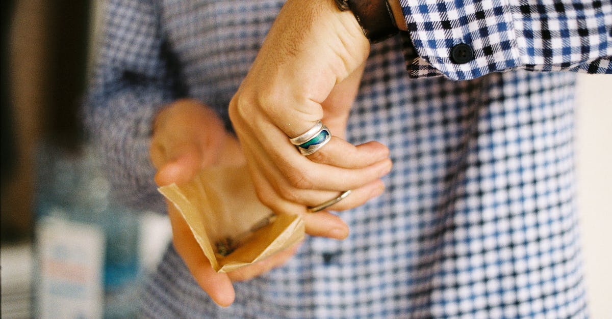 Why isn't my paper mill being provided with lumber? - Crop unrecognizable male in checkered shirt holding parchment paper with cannabis and milling hemp with scissors while standing in daylight