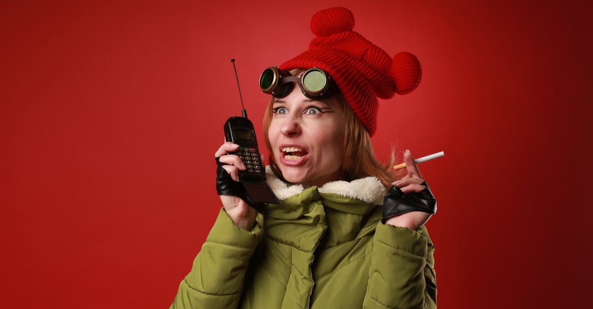 Why use the existing radio tower? - Surprised female model in outerwear with cigarette talking into portable transceiver while looking away on red background