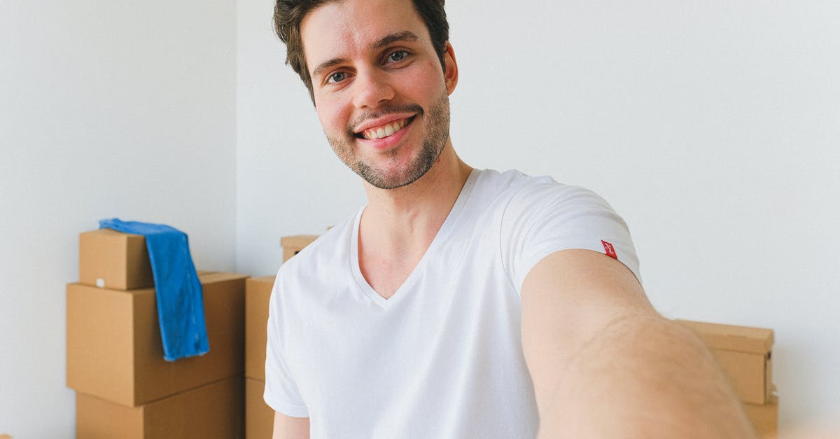 Why won't the NPC move in? [duplicate] - Delighted young relocating man with dark hair in white t shirt smiling and looking at camera while taking selfie against pile of cardboard boxes in new purchased apartment