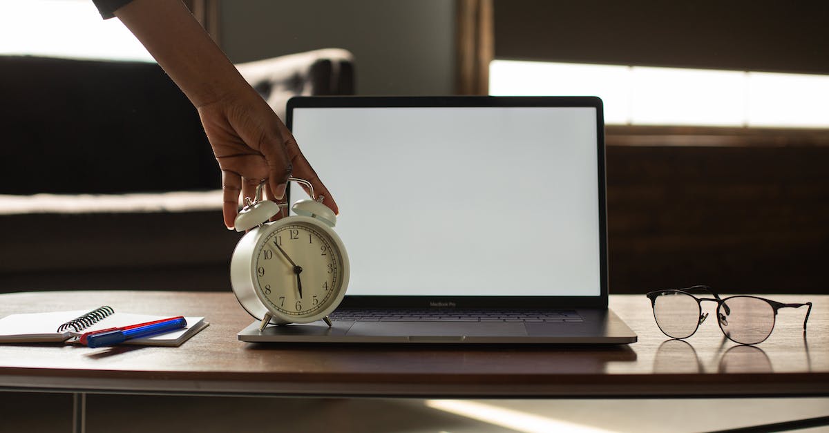 Why won't the time show at the Island? - Anonymous black person touching alarm clock near opened netbook with white blank screen placed on table with notebook and pens