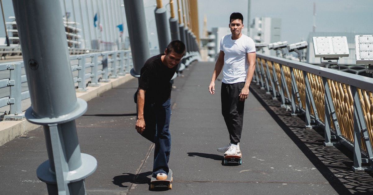 Will moving iron golems allow more to spawn? - Full body of young ethnic men skateboarding on asphalt bridge with metal constructions under cloudy sky