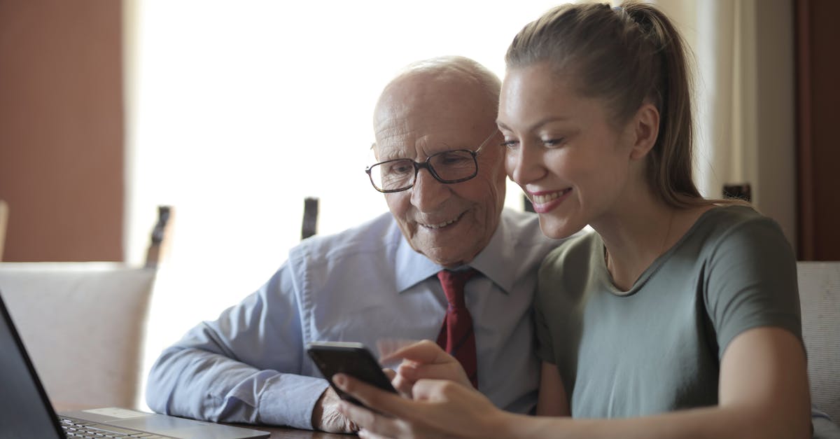 Will my Rust character differ if not using family sharing? - Smiling young woman in casual clothes showing smartphone to interested senior grandfather in formal shirt and eyeglasses while sitting at table near laptop