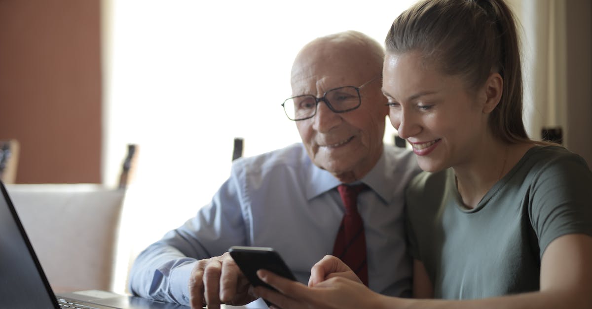 Will my Rust character differ if not using family sharing? - Positive senior man in formal shirt and eyeglasses and smiling young granddaughter sharing mobile phone while sitting near laptop at table