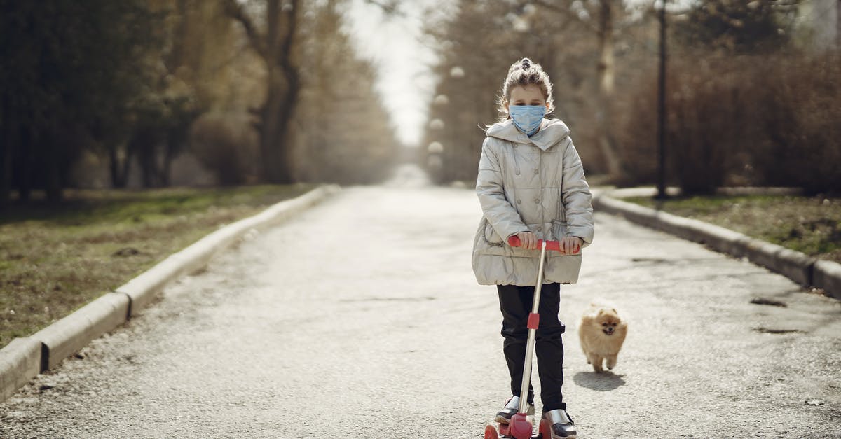Will riding a rock dog allow me to walk in lava pits? - Full body full length of cute little girl in disposable mask riding scooter near funny dog running on pavement in autumn forest