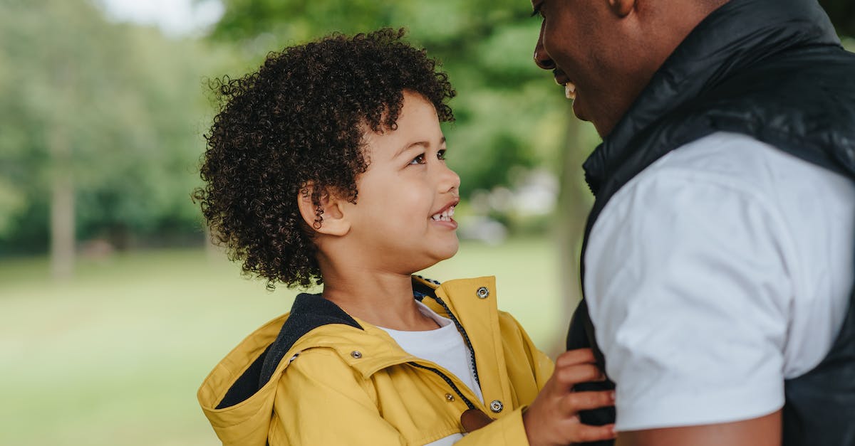 Will wearing special outfits during smile time affect a child? - Side view of crop smiling African American father talking to charming child on street while looking at each other