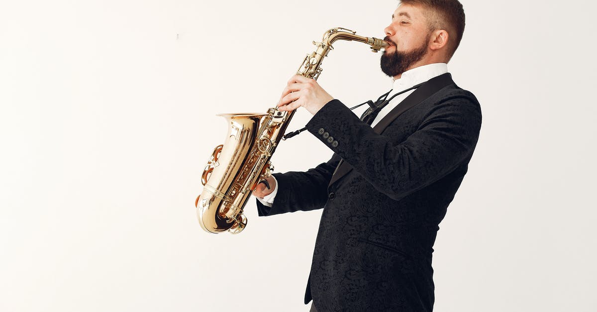 XBOX Live Gold Sharing - Side view of professional male musician wearing concert costume playing music on saxophone standing against white background in studio with passion and inspiration